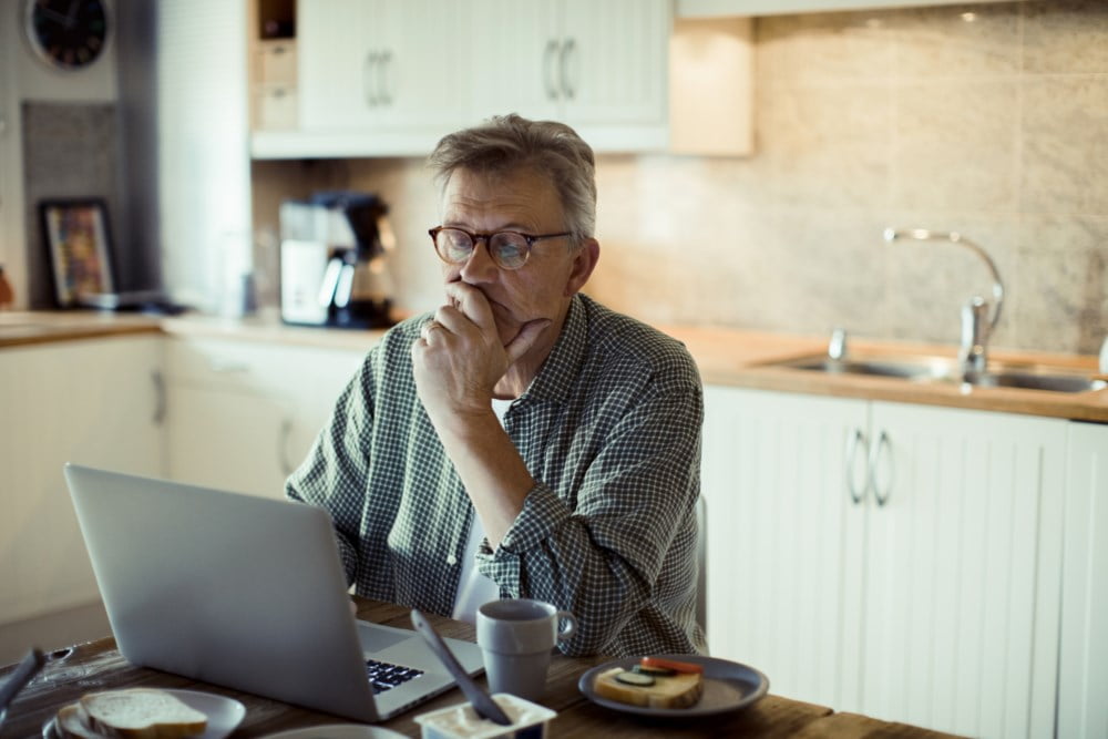 Mann som sitter på kjøkken foran en laptop